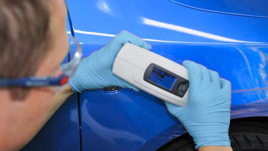 Technician using a handheld paint thickness gauge on a blue car panel to assess coating uniformity and finish quality at ProFinish Supply in West Palm Beach